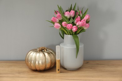 Photo of Bouquet of beautiful tulips in vase, LED lamp and decorative pumpkin on wooden table near grey wall