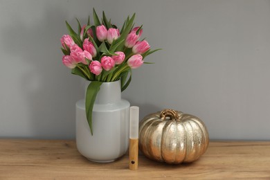 Photo of Bouquet of beautiful tulips in vase, LED lamp and decorative pumpkin on wooden table near grey wall