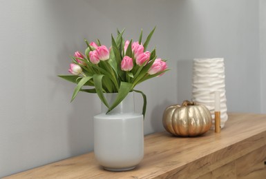 Photo of Bouquet of beautiful tulips in vase, LED lamp and decorative pumpkin on wooden cabinet near grey wall indoors