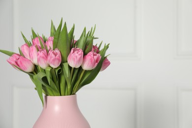 Photo of Bouquet of beautiful tulips in vase near white wall indoors, closeup. Space for text