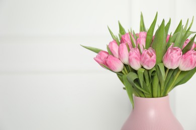 Photo of Bouquet of beautiful tulips in vase near white wall indoors, closeup. Space for text