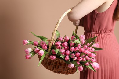 Photo of Woman holding wicker basket with bouquet of beautiful tulips on dark beige background, closeup