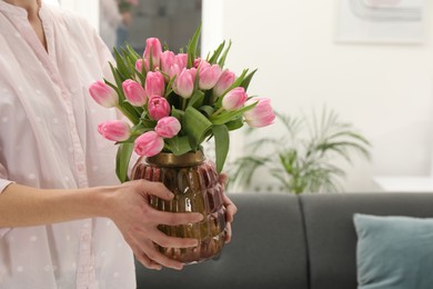 Photo of Woman holding vase with bouquet of beautiful tulips indoors, closeup. Space for text