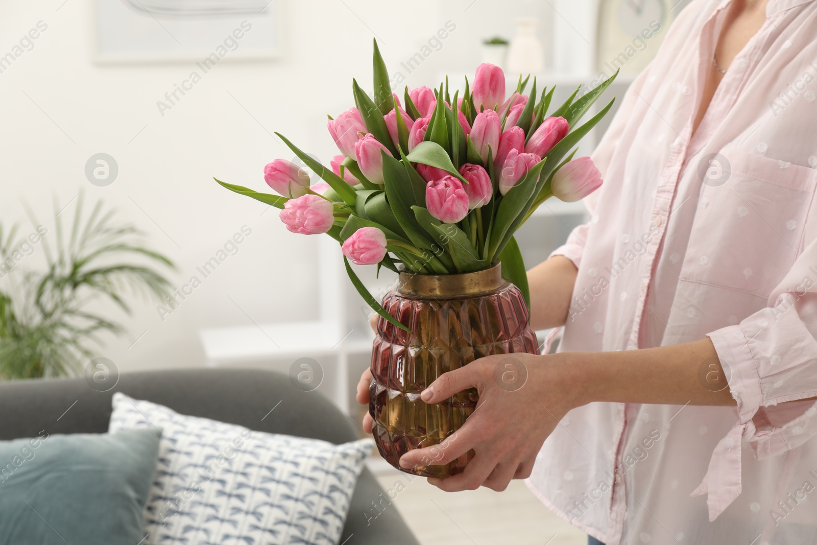 Photo of Woman holding vase with bouquet of beautiful tulips indoors, closeup. Space for text