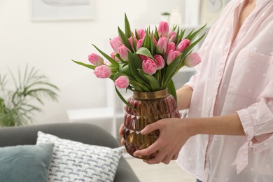 Photo of Woman holding vase with bouquet of beautiful tulips indoors, closeup. Space for text