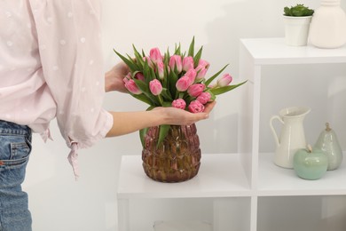 Photo of Woman with bouquet of beautiful tulips near shelving unit indoors, closeup