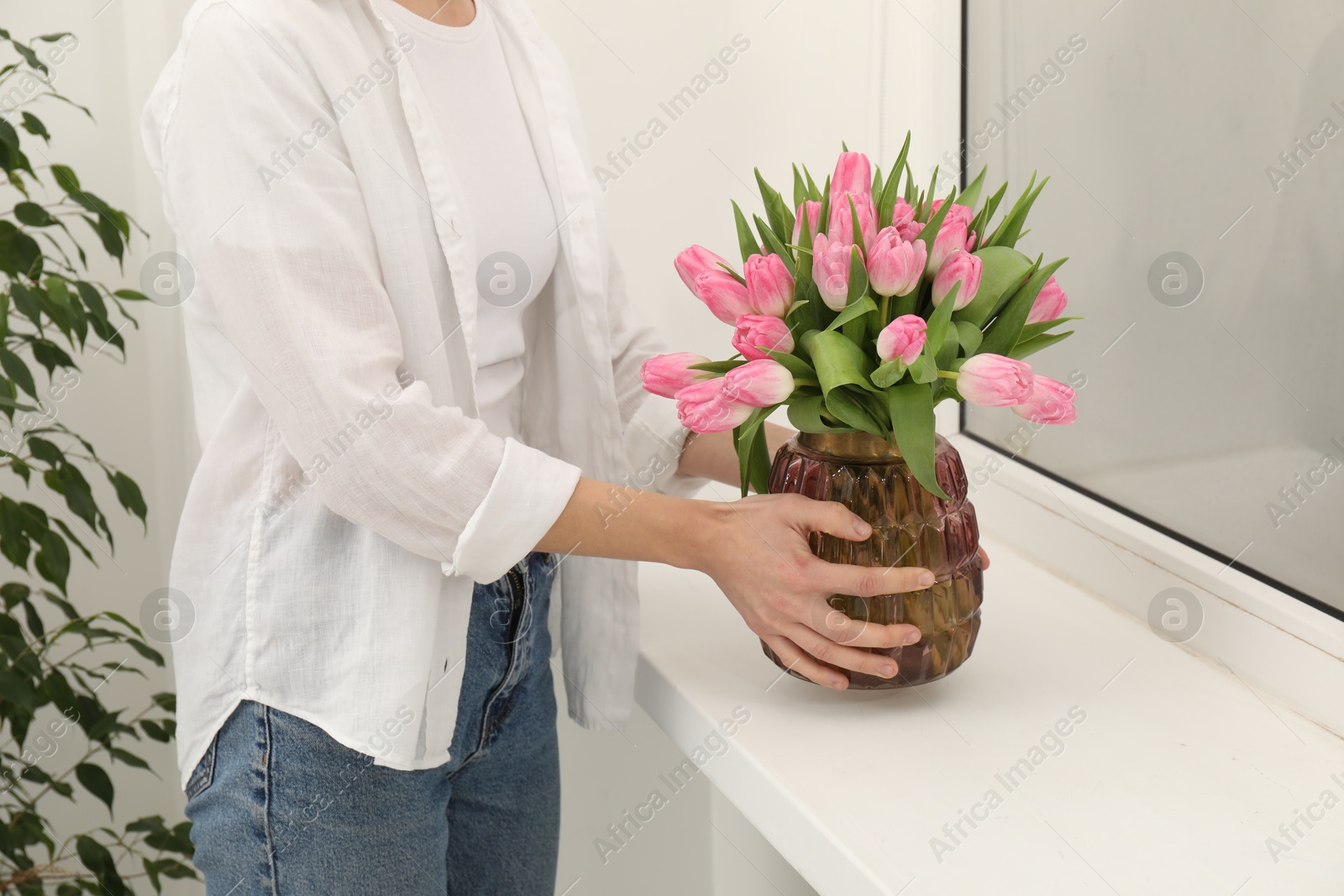 Photo of Woman arranging vase with bouquet of beautiful tulips onto window sill indoors, closeup