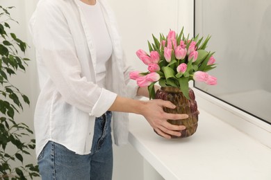 Photo of Woman arranging vase with bouquet of beautiful tulips onto window sill indoors, closeup