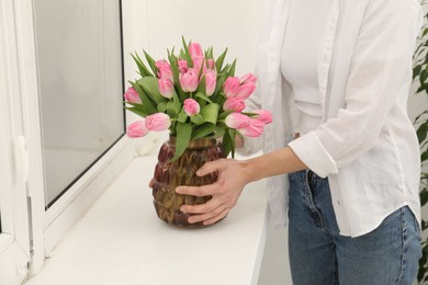 Photo of Woman arranging vase with bouquet of beautiful tulips onto window sill indoors, closeup