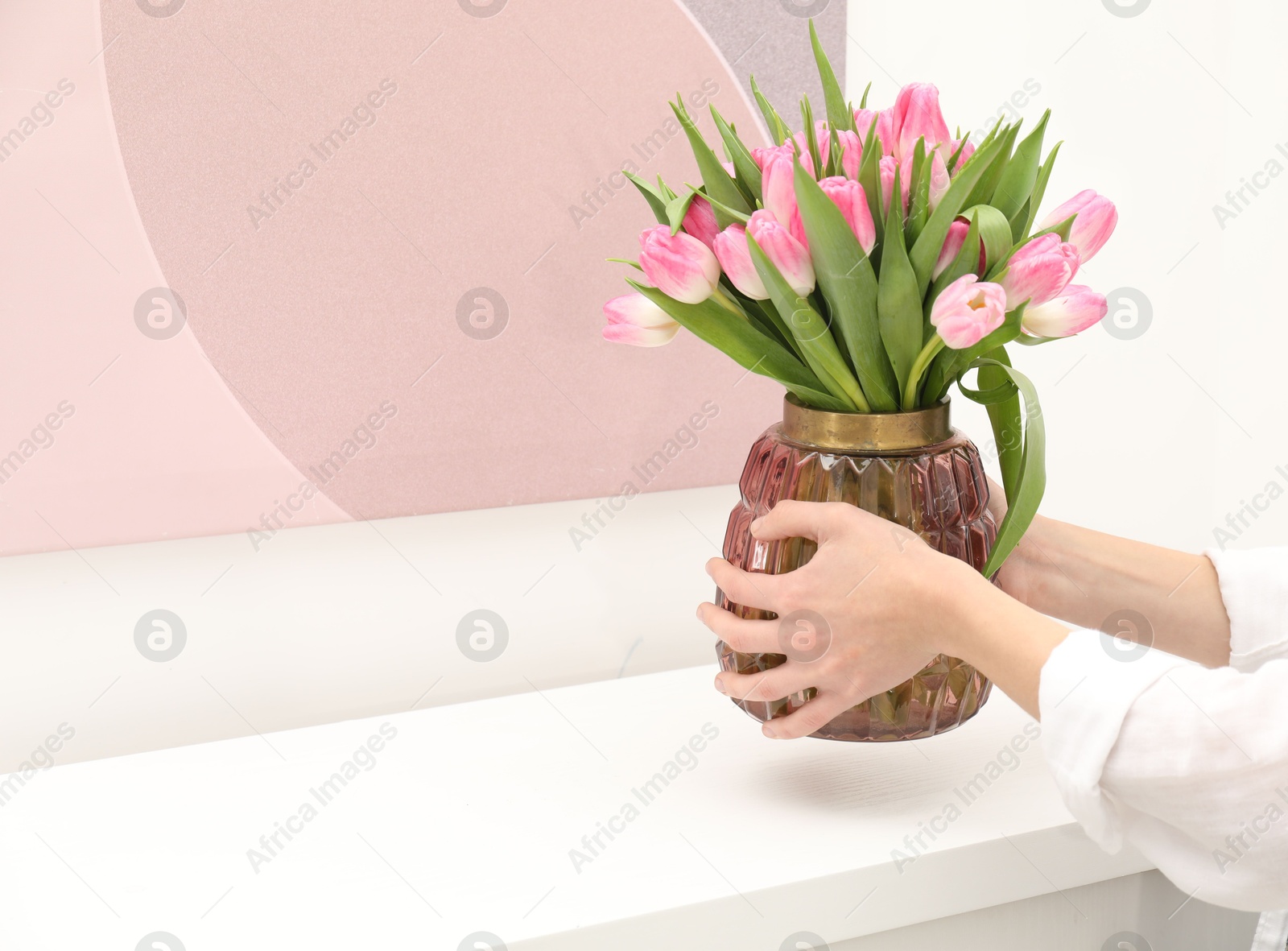 Photo of Woman arranging vase with bouquet of beautiful tulips onto window sill indoors, closeup. Space for text