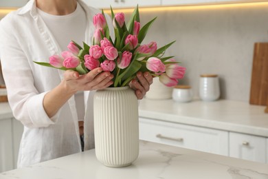 Photo of Woman with bouquet of beautiful tulips at white marble table in kitchen, closeup. Space for text