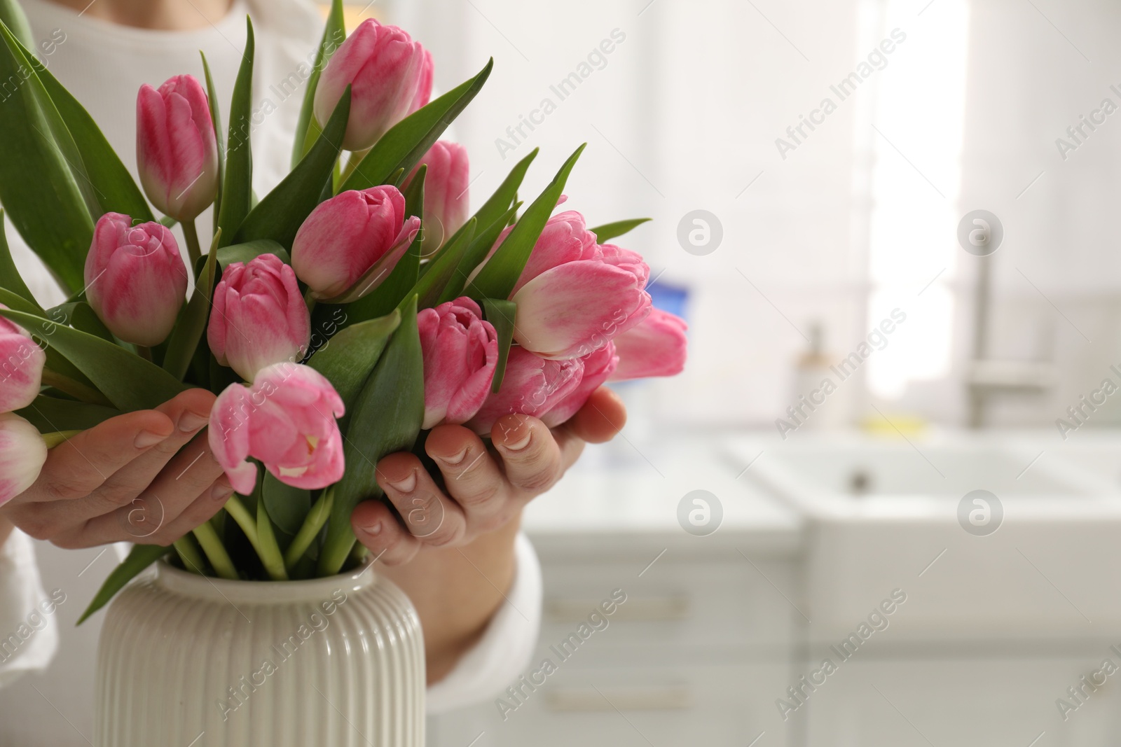 Photo of Woman with bouquet of beautiful tulips in kitchen, closeup. Space for text