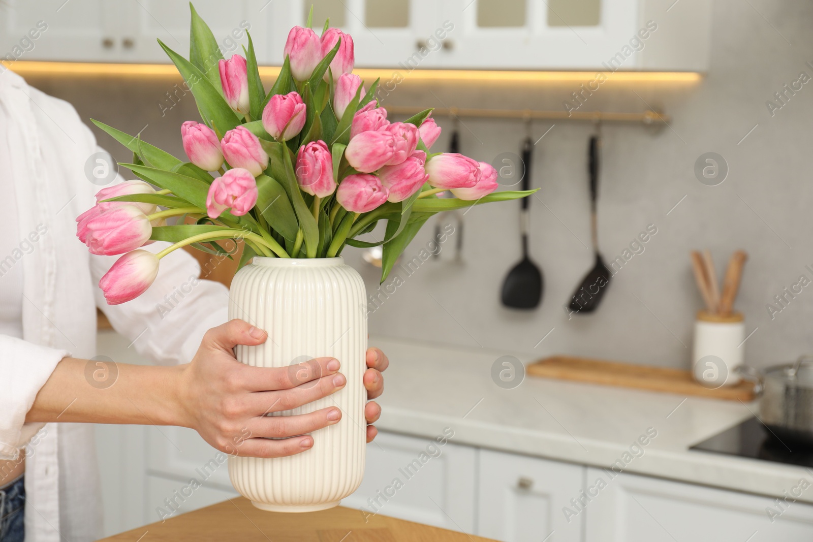 Photo of Woman holding vase with bouquet of beautiful tulips in kitchen, closeup. Space for text