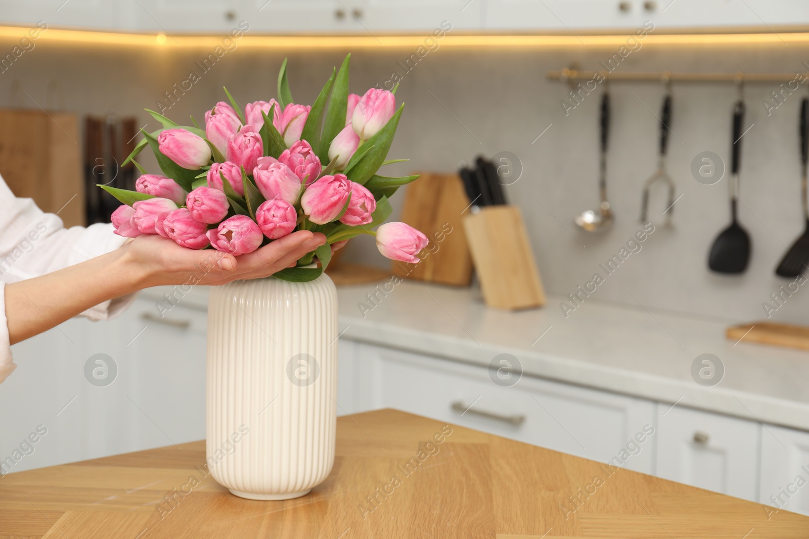 Photo of Woman with bouquet of beautiful tulips at wooden table in kitchen, closeup. Space for text