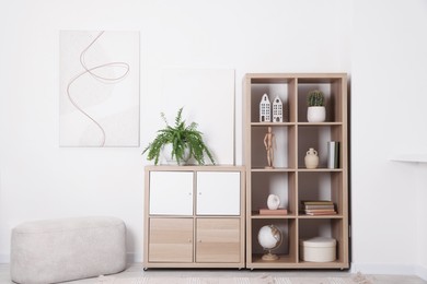 Photo of Shelving unit with different home decor, houseplant and ottoman near white wall indoors