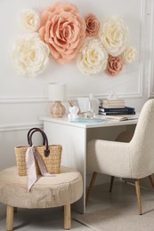 Photo of Beautiful decorative paper flowers on white wall and stylish furniture indoors