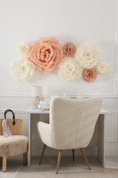 Photo of Beautiful decorative paper flowers on white wall and stylish furniture indoors