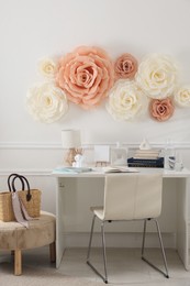 Beautiful decorative paper flowers on white wall and stylish furniture indoors