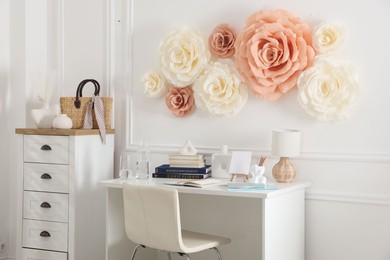 Beautiful decorative paper flowers on white wall and stylish furniture indoors