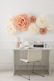 Photo of Beautiful decorative paper flowers on white wall and stylish furniture indoors