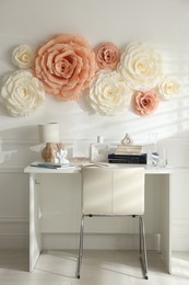 Beautiful decorative paper flowers on white wall and stylish furniture indoors