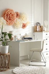 Photo of Beautiful decorative paper flowers on white wall and stylish furniture indoors