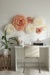 Beautiful decorative paper flowers on white wall and stylish furniture indoors