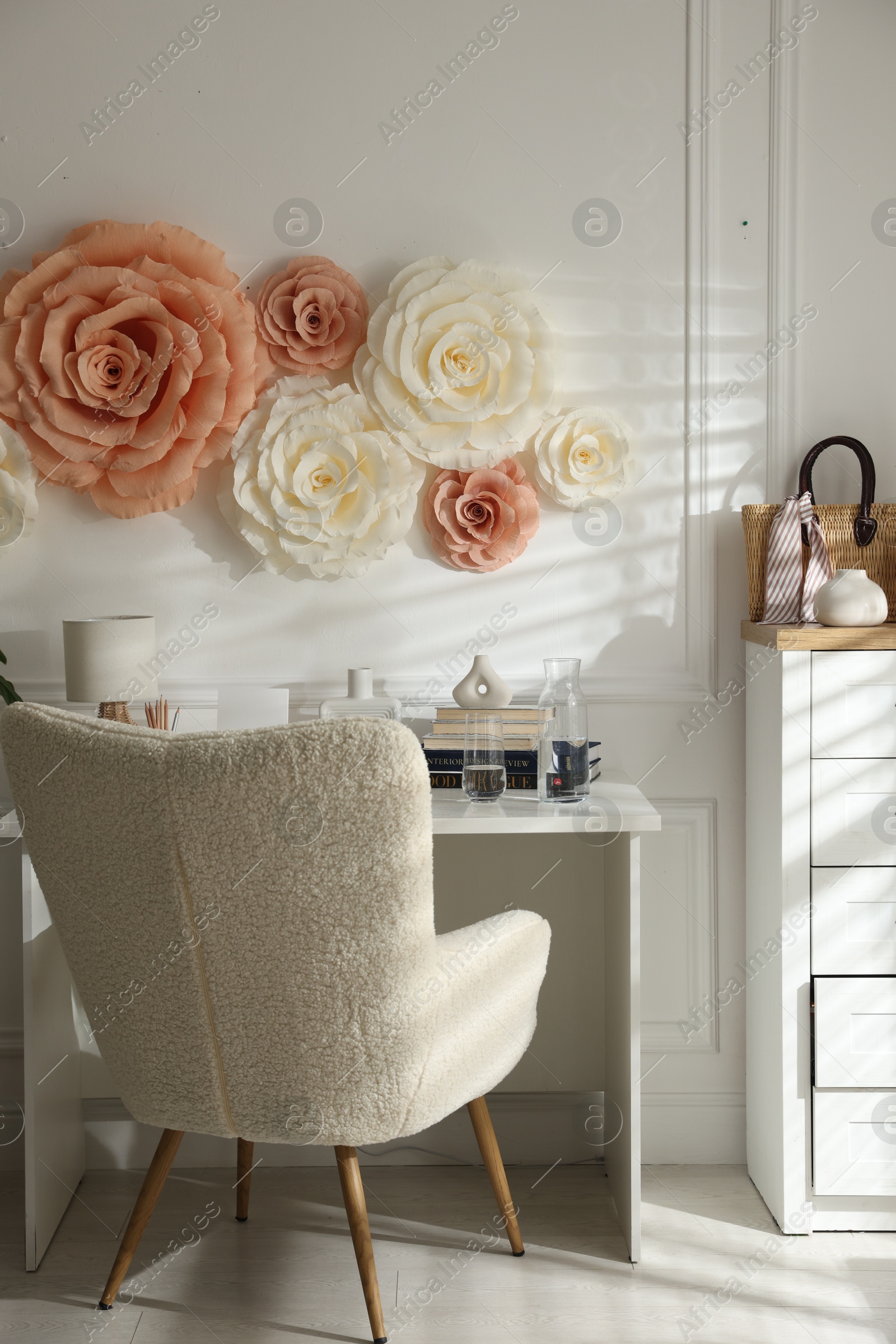 Photo of Beautiful decorative paper flowers on white wall and stylish furniture indoors