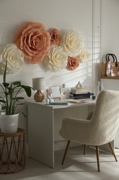 Beautiful decorative paper flowers on white wall and stylish furniture indoors