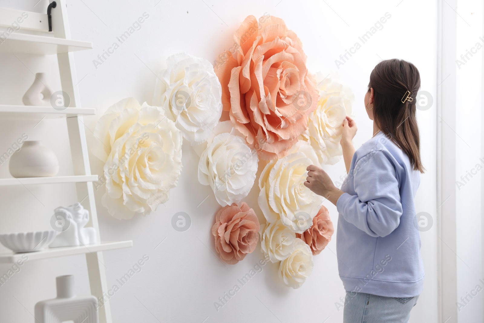 Photo of Woman decorating wall with beautiful paper flowers at home