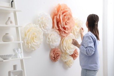 Woman decorating wall with beautiful paper flowers at home