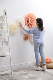 Woman decorating wall with beautiful paper flowers at home