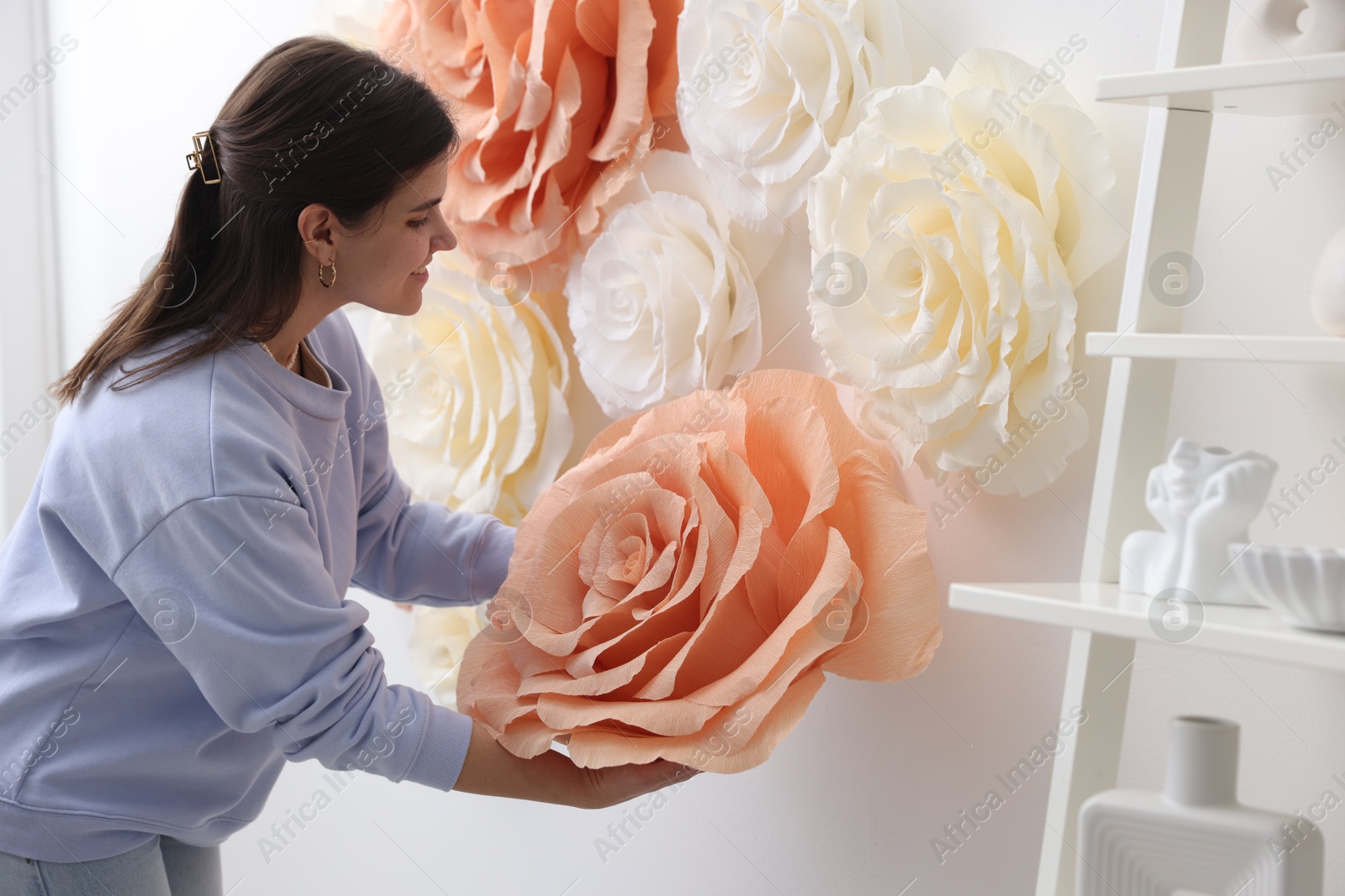 Photo of Smiling woman decorating wall with beautiful paper flowers at home