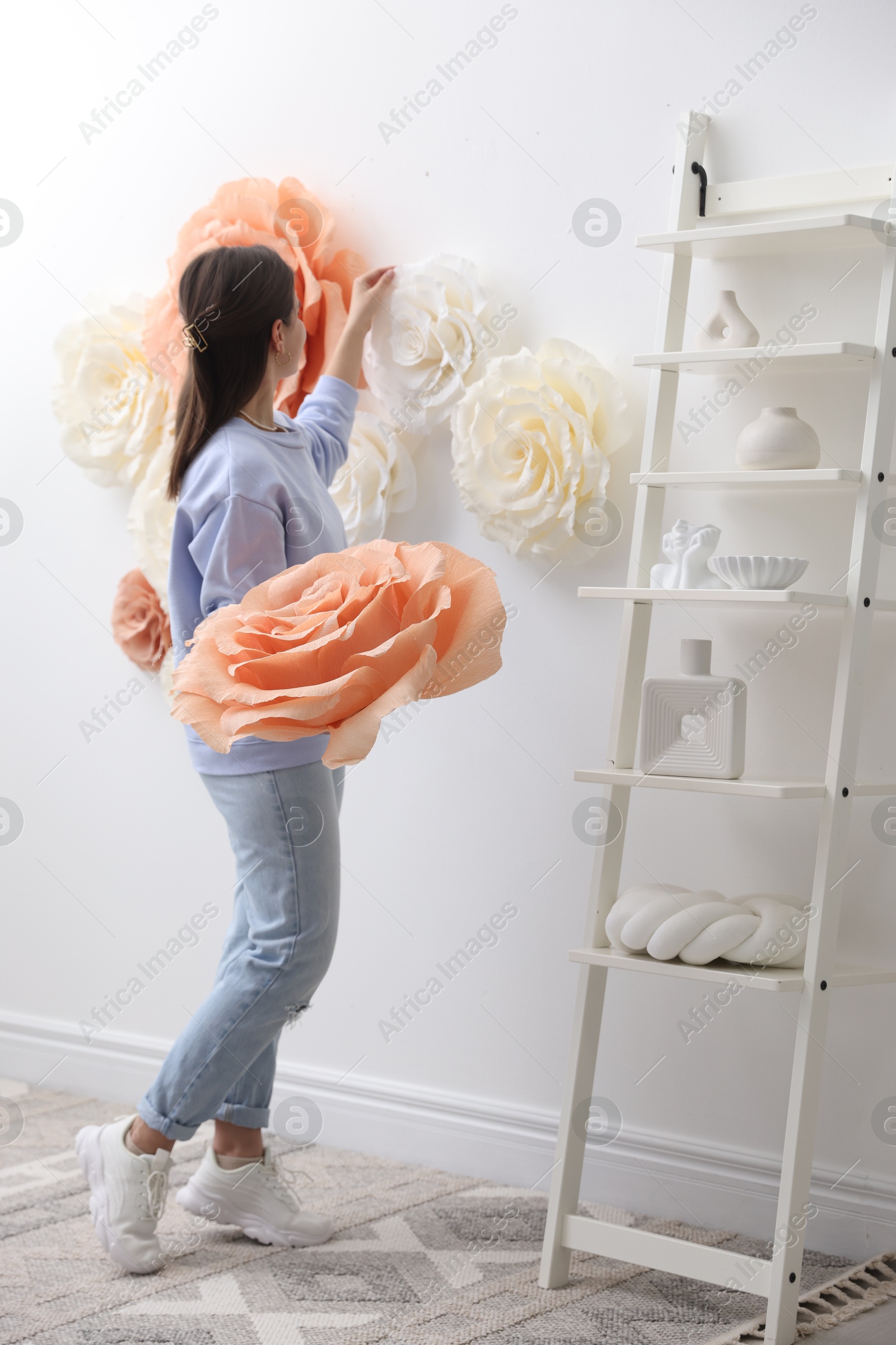 Photo of Woman decorating wall with beautiful paper flowers at home