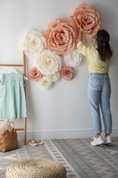 Photo of Woman decorating wall with beautiful paper flowers at home, back view