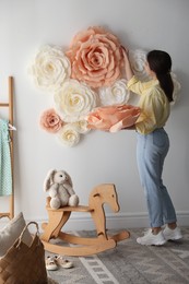 Woman decorating wall with beautiful paper flowers in child's room