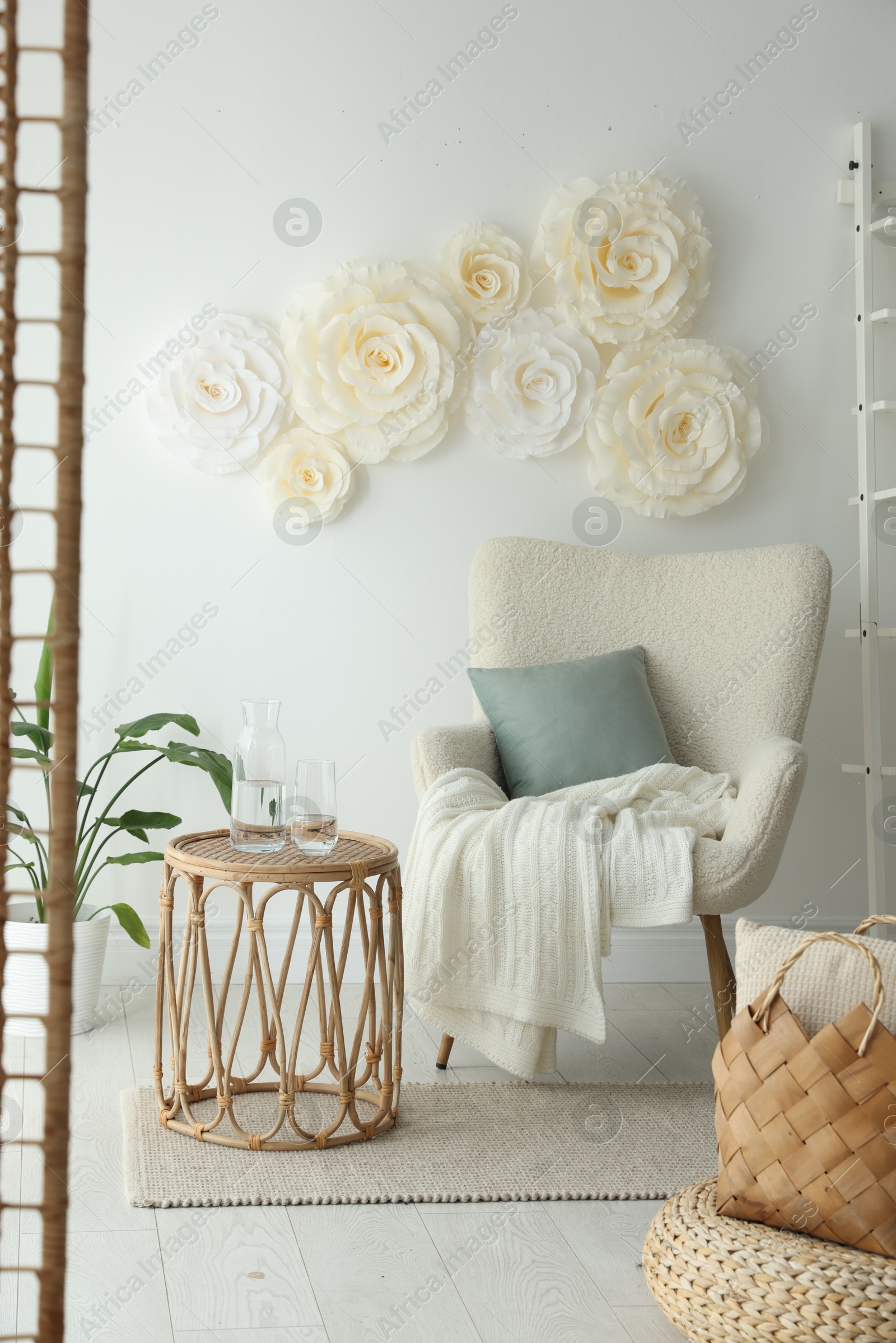 Photo of Beautiful decorative paper flowers on white wall and stylish furniture indoors