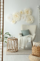 Beautiful decorative paper flowers on white wall and stylish furniture indoors