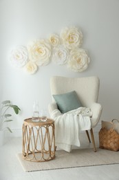 Photo of Beautiful decorative paper flowers on white wall and stylish furniture indoors