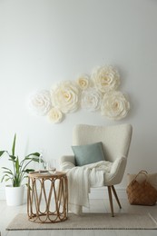 Beautiful decorative paper flowers on white wall and stylish furniture indoors