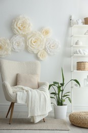 Beautiful decorative paper flowers on white wall and stylish furniture indoors