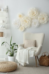 Photo of Beautiful decorative paper flowers on white wall and stylish furniture indoors