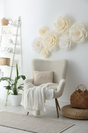 Beautiful decorative paper flowers on white wall and stylish furniture indoors