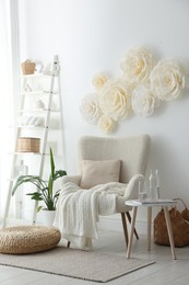 Photo of Beautiful decorative paper flowers on white wall and stylish furniture indoors