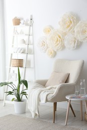 Photo of Beautiful decorative paper flowers on white wall and stylish furniture indoors