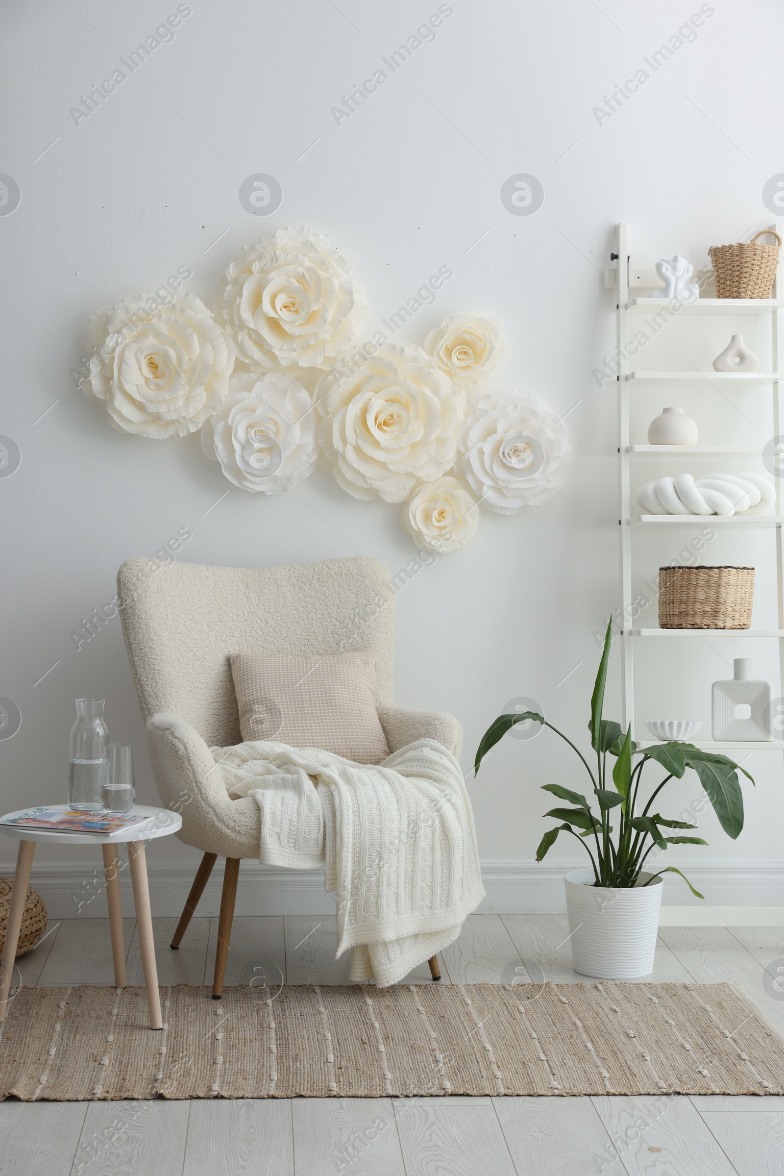 Photo of Beautiful decorative paper flowers on white wall and stylish furniture indoors