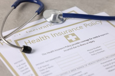 Photo of Health insurance policy forms and stethoscope on grey table, closeup