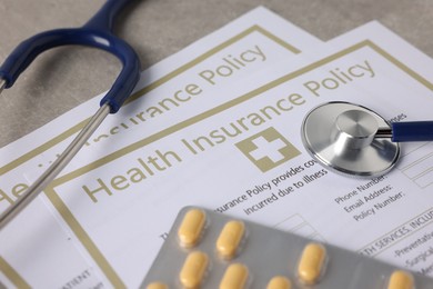 Photo of Health insurance policy forms, pills and stethoscope on grey table, closeup