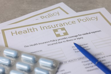 Photo of Health insurance policy forms, pills and pen on grey table, closeup