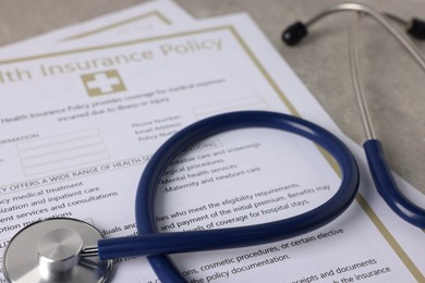 Photo of Health insurance policy forms and stethoscope on grey table, closeup